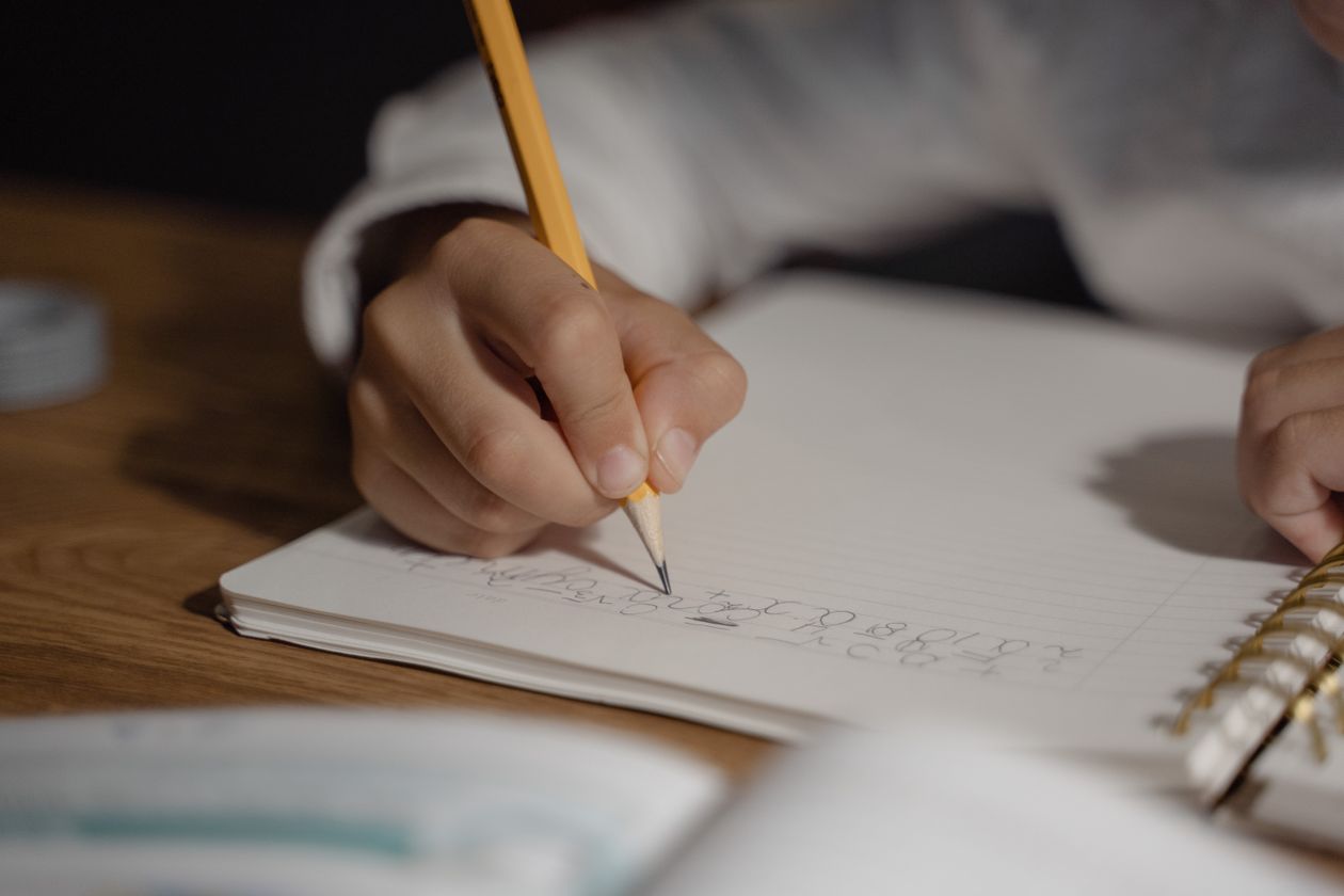 Child writing homework in a spiral notebook with a pencil