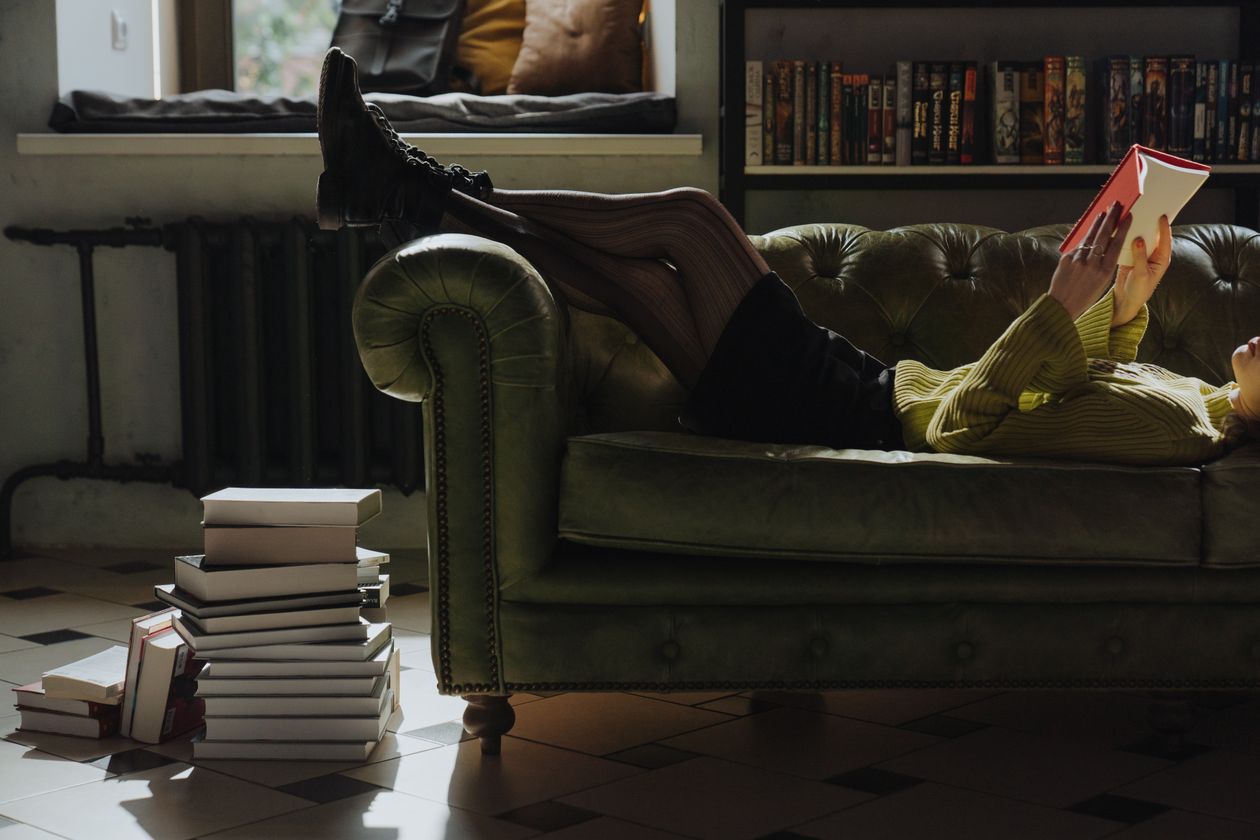 Reader stretched out on a green sofa absorbed in a book