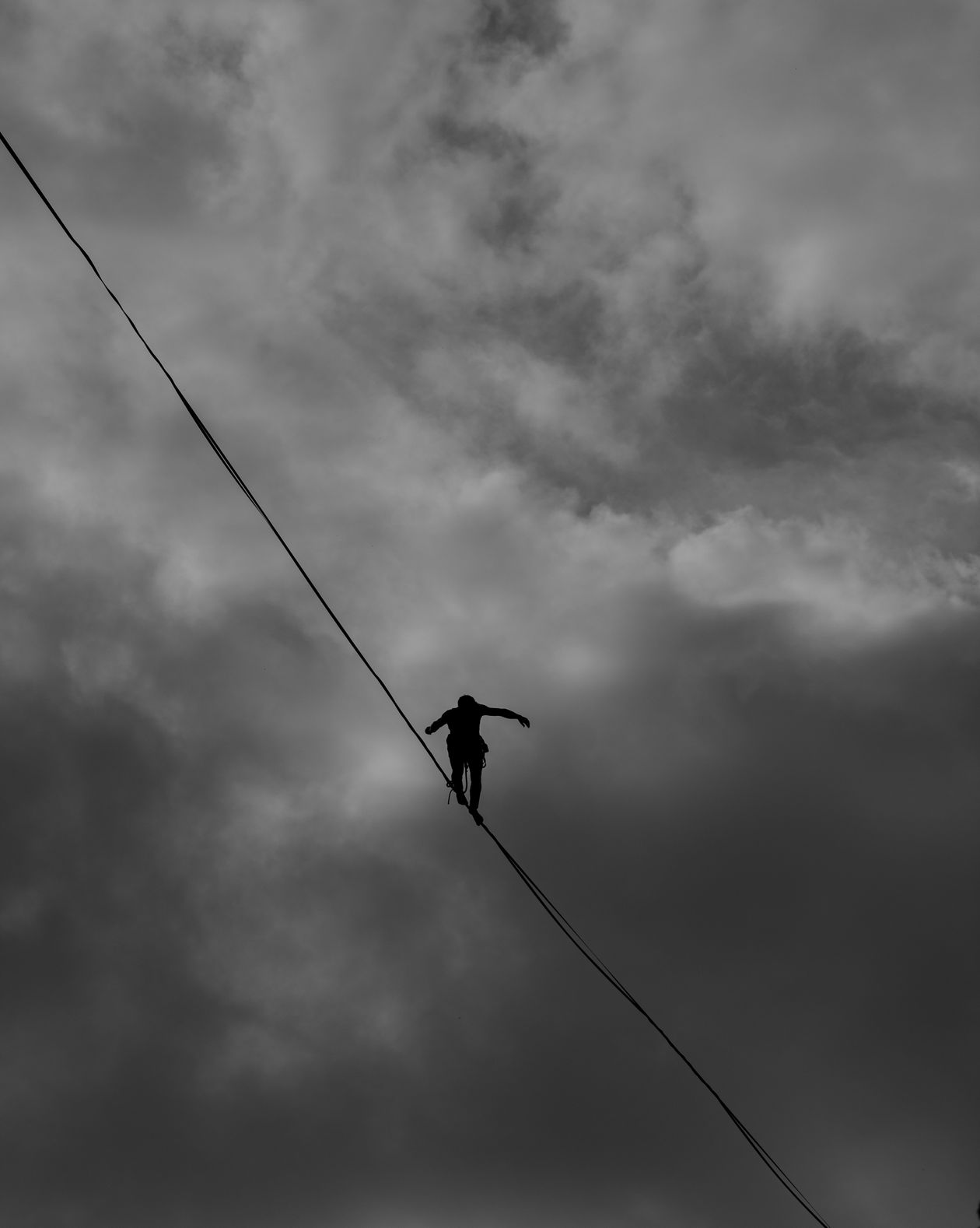 Silhouette of a tightrope walker balancing against a stormy sky